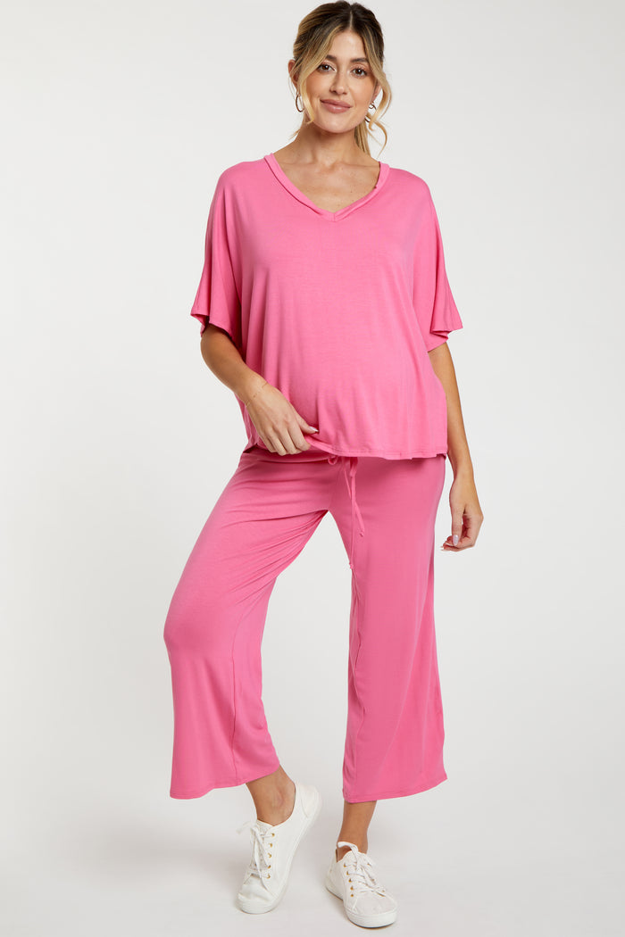 woman wearing a pink maternity top and matching pants, relaxed fit with a v-neck and loose sleeves, showcasing a baby bump