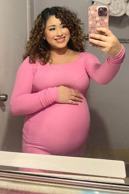 woman wearing a fitted pink long sleeve maternity dress with her baby bump visible, taking a selfie in the mirror