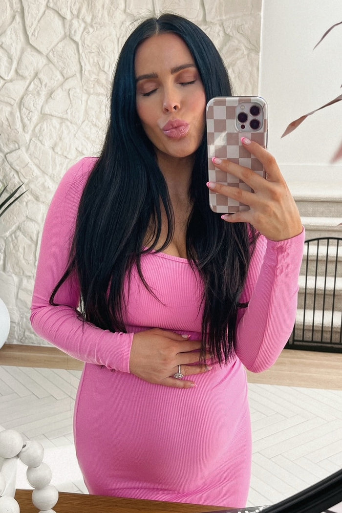 woman wearing a pink long sleeve maternity dress and holding her baby bump