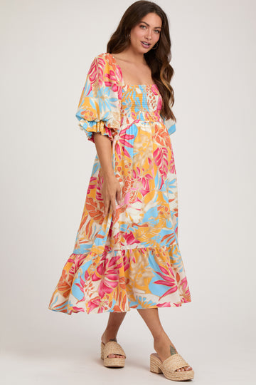 woman wearing a colorful floral maternity dress with smocked bodice and ruffle hem, showing her baby bump