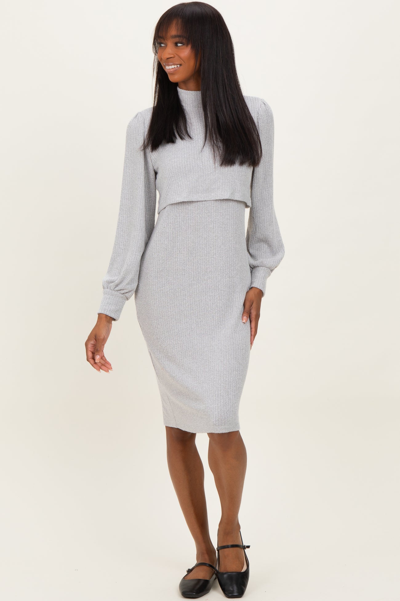 woman wearing a gray two-piece dress with long sleeves and a fitted skirt, posing and smiling