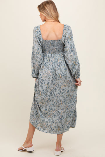 woman wearing a light blue floral print maternity dress with smocked bodice and long sleeves, showing her back