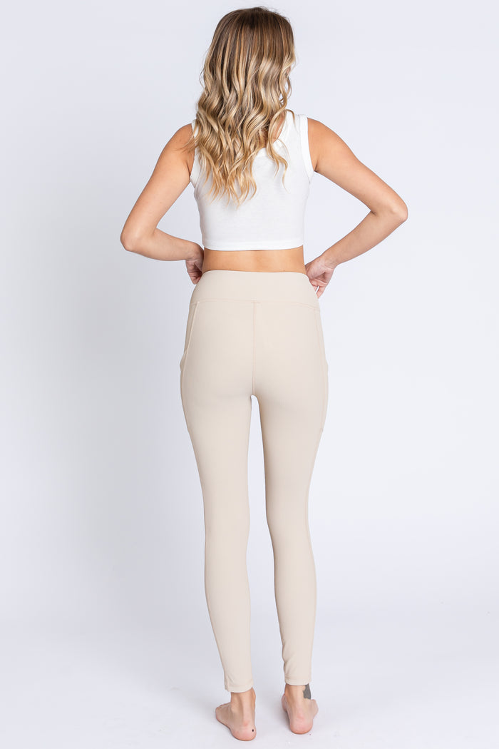 woman wearing a white cropped tank top and beige high-waisted leggings, shown from the back