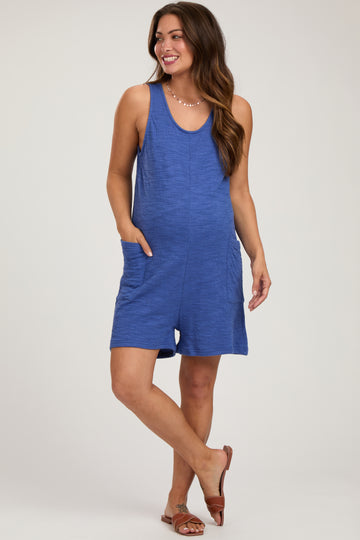 woman wearing a blue tank style maternity romper with side pockets and a visible baby bump