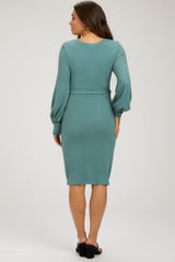 woman wearing a teal maternity dress with long puff sleeves and a fitted waist, showcasing her baby bump from the back