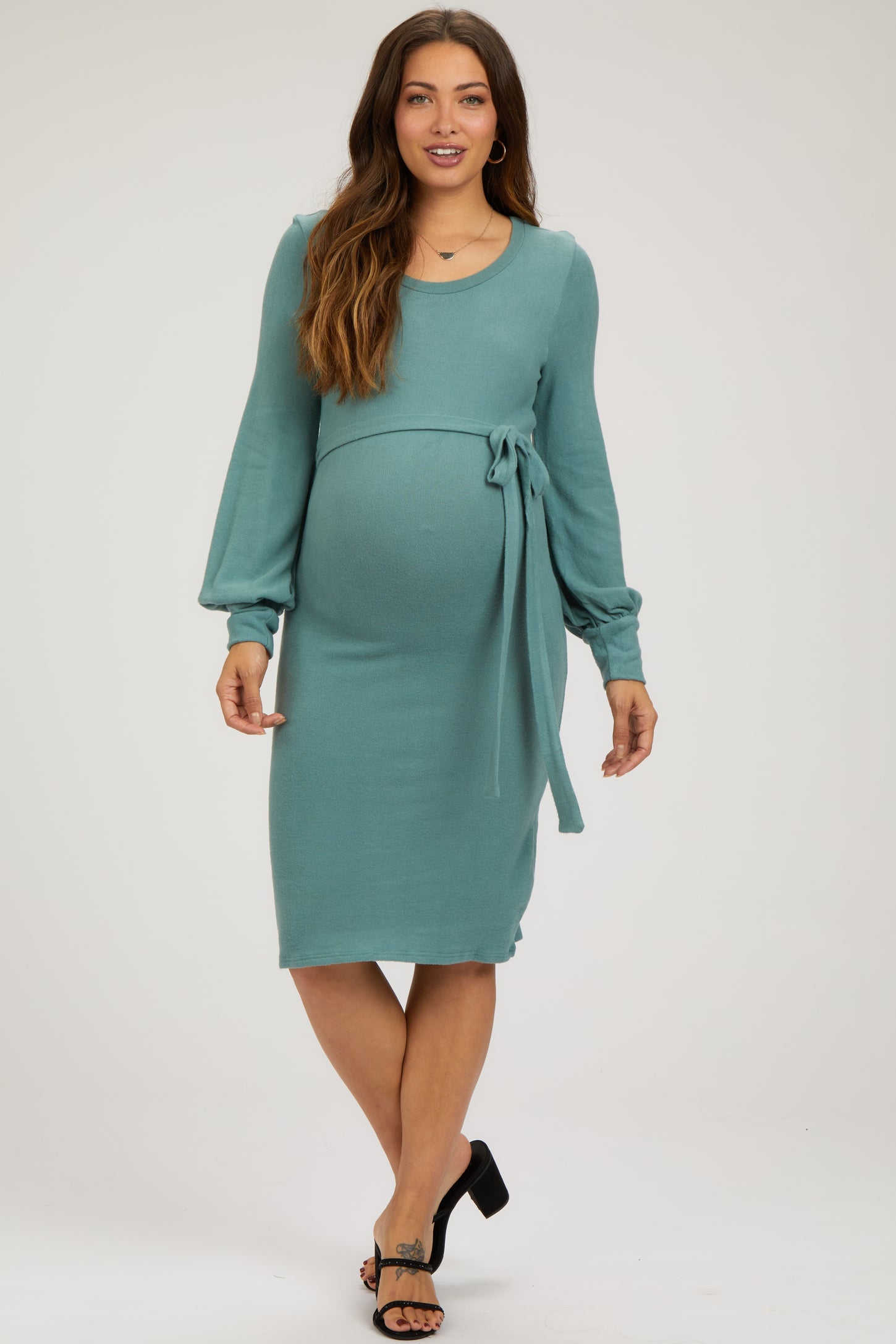 woman wearing a teal maternity dress with long sleeves and a waist tie, showcasing her baby bump