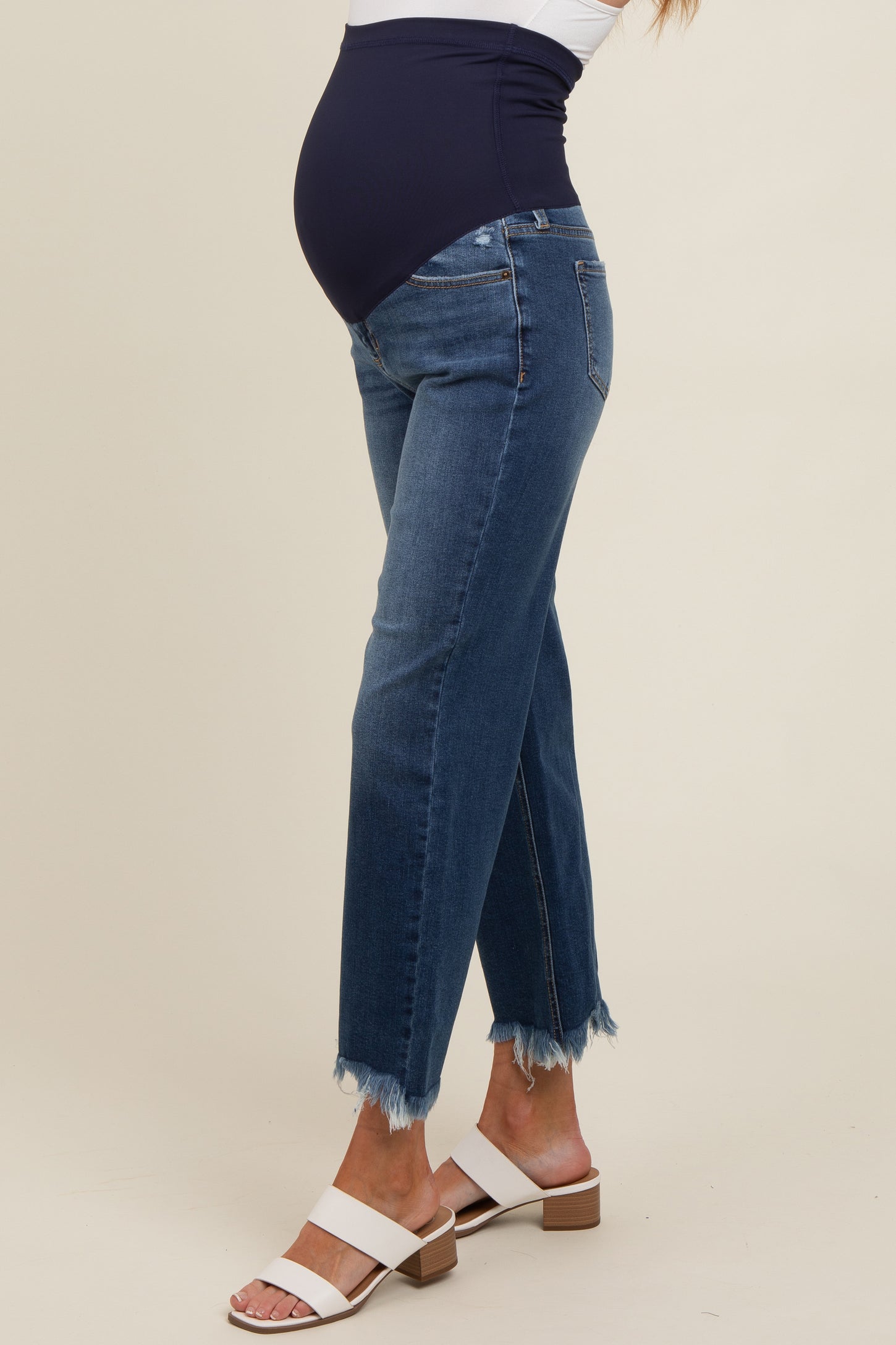 woman wearing dark blue maternity jeans with a frayed hem and a supportive over-the-bump waistband, showing her baby bump