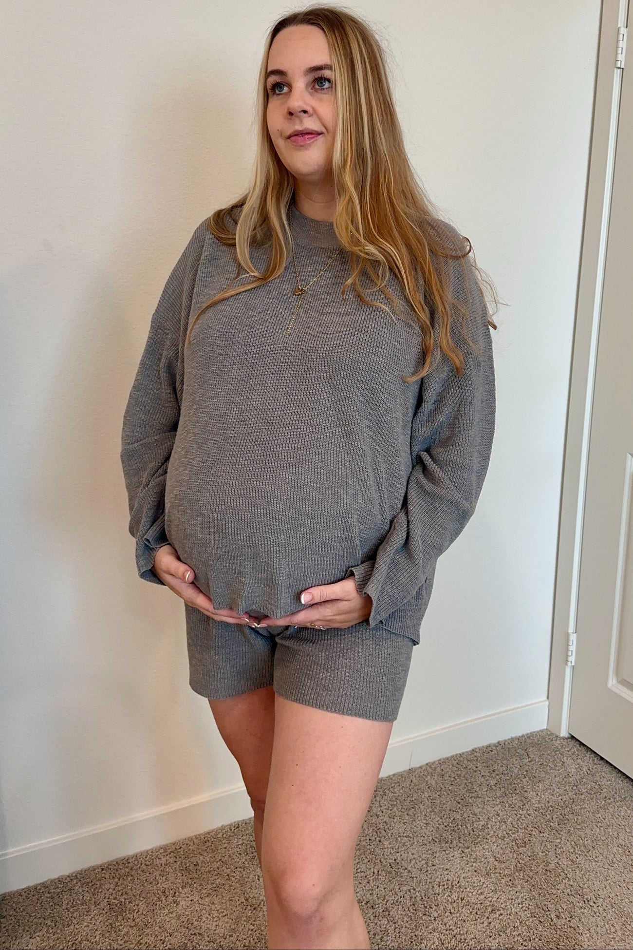woman wearing a gray ribbed maternity loungewear set with a long sleeve top and shorts, holding her baby bump