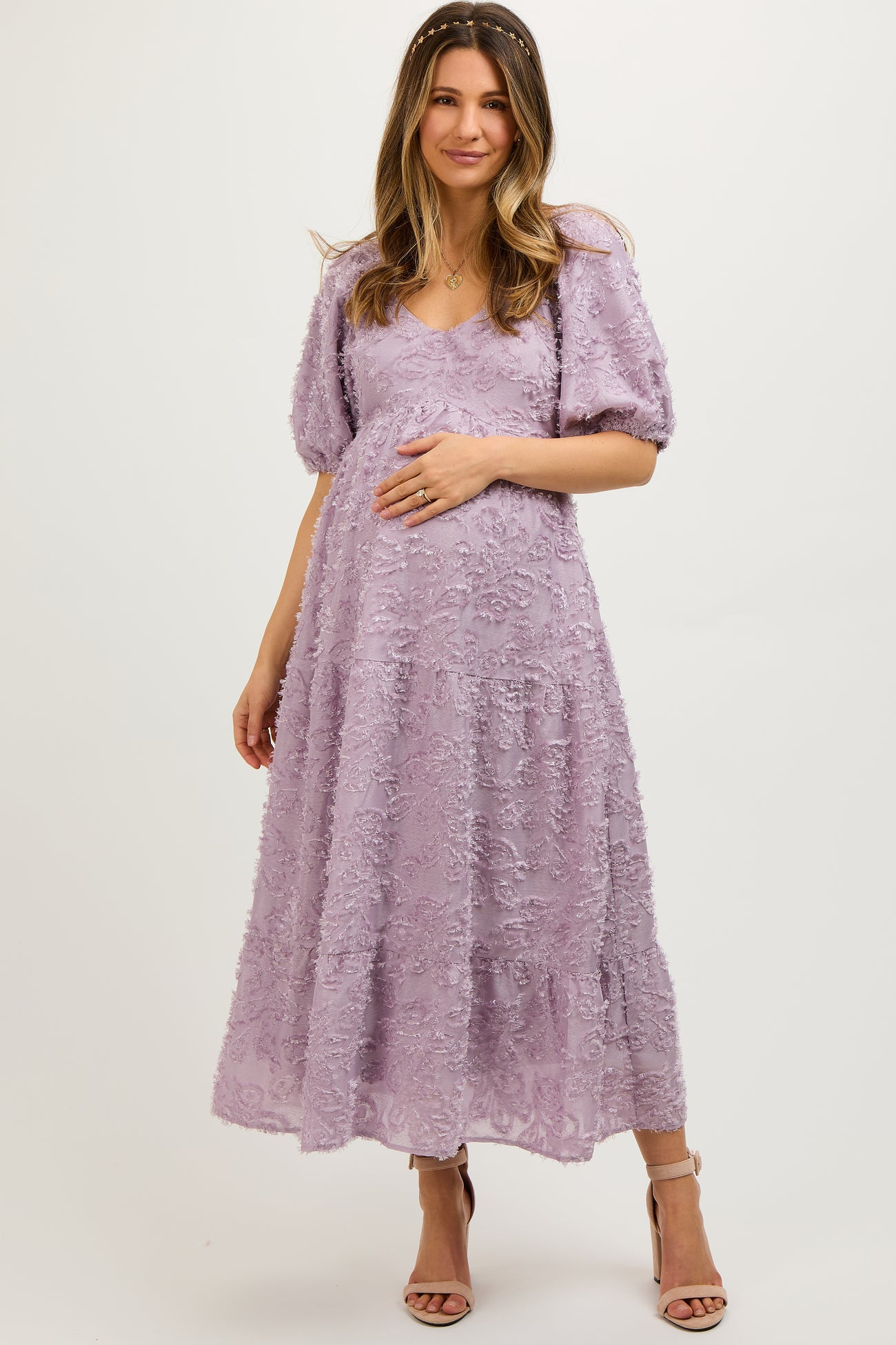 woman wearing a lavender maternity dress with floral embroidery and puff sleeves, gently cradling her baby bump