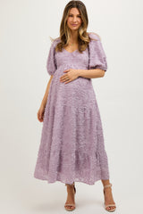 woman wearing a lavender maternity dress with floral embroidery and puff sleeves, gently cradling her baby bump
