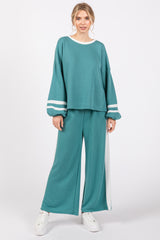 woman wearing a teal oversized sweatshirt with white stripes and matching wide-leg pants