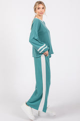 woman wearing a teal two-piece lounge set with white stripe details on sleeves and pants, paired with white sneakers