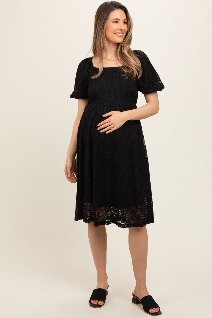 woman wearing a black lace maternity dress, smiling and holding her baby bump