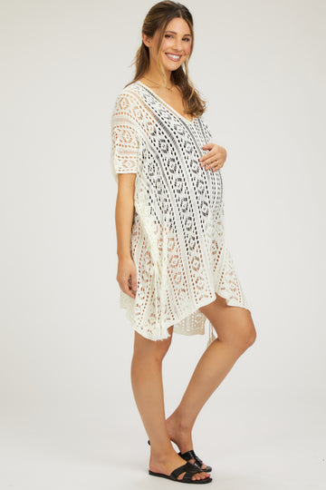 woman wearing a white lace maternity cover-up dress and holding her baby bump