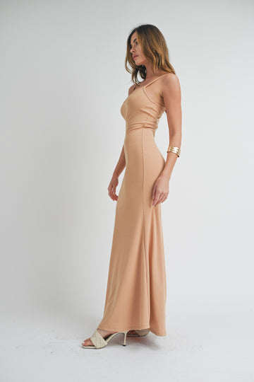 woman wearing a nude fitted maxi dress with ribbed texture and a side slit, standing in profile against a neutral background