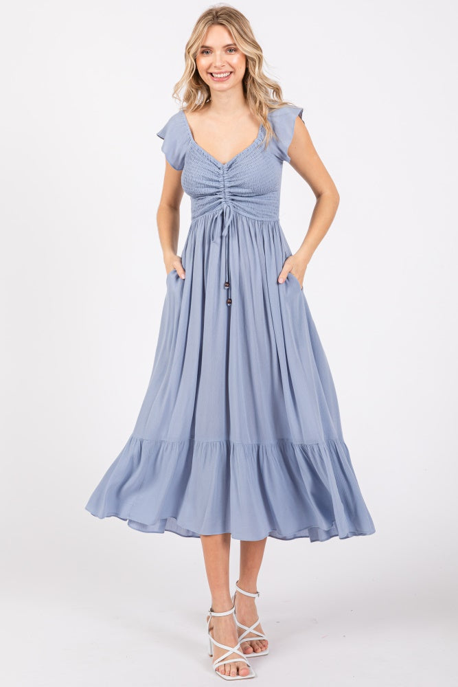 woman wearing a light blue maxi dress with flutter sleeves and a cinched waist, styled with pockets