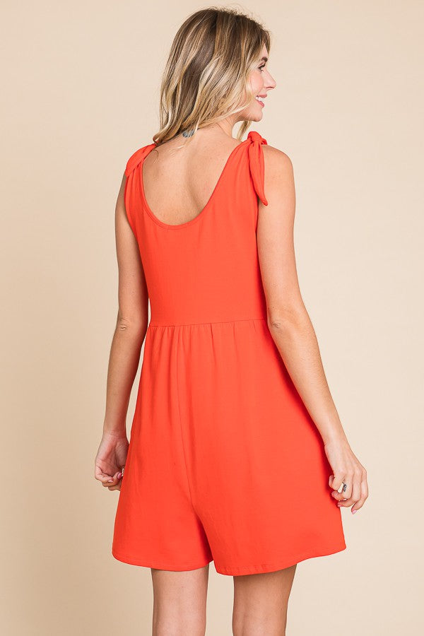 woman wearing a bright orange sleeveless romper with tie straps and a fitted waist, showing the back view