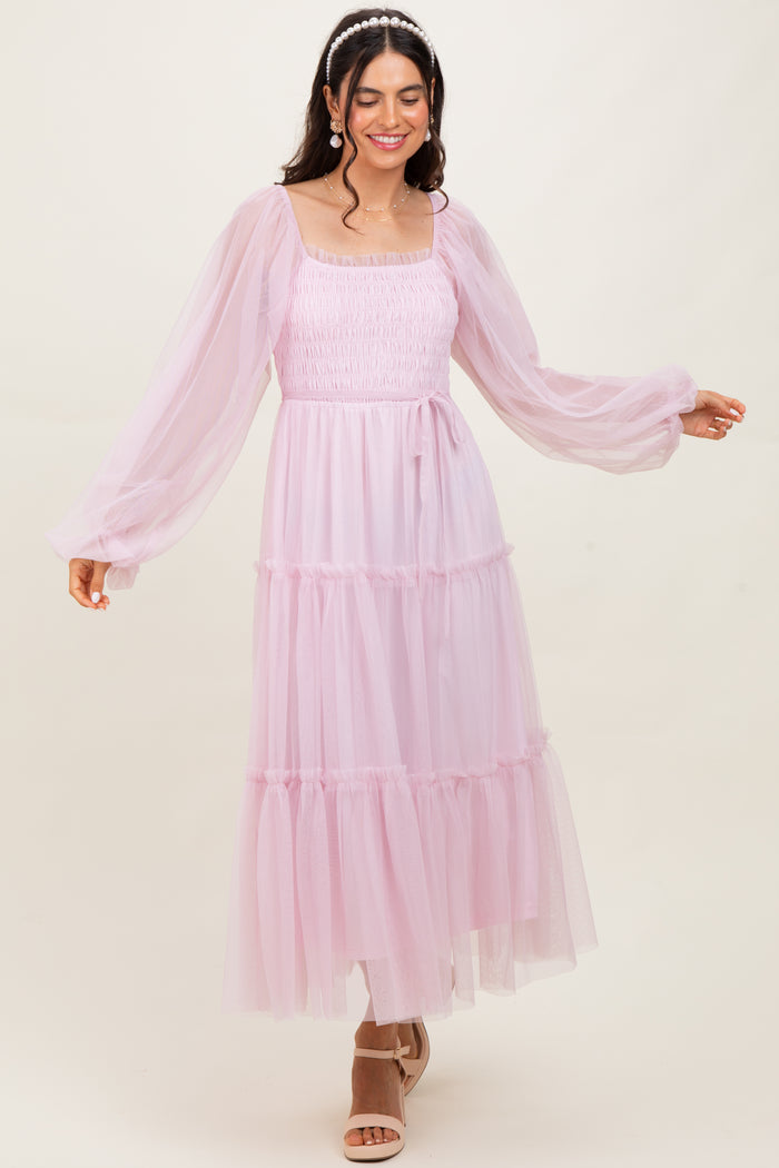 woman wearing a light pink tiered tulle maxi dress with long sleeves and a square neckline