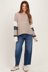 woman wearing a beige maternity sweater with navy and white stripes and blue wide-leg jeans, showing her baby bump