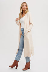 woman wearing a long beige cardigan over a white top and blue jeans, paired with brown ankle boots