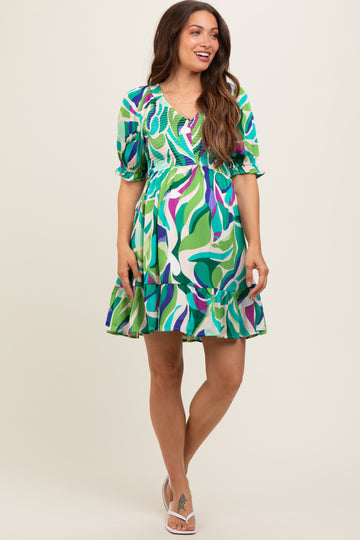 woman wearing a vibrant green and purple floral print maternity dress with puff sleeves and a flared hemline