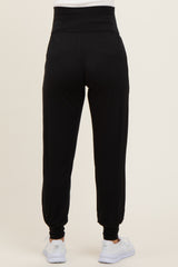 woman wearing black maternity joggers with a high waistband and cuffed ankles, view from the back
