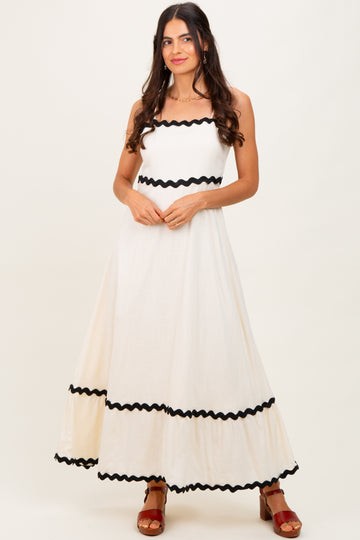 woman wearing a cream maxi dress with black ric rac trim and a fitted bodice