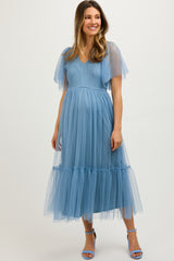 woman wearing a light blue maternity dress with sheer flutter sleeves and tiered tulle skirt, showing her baby bump
