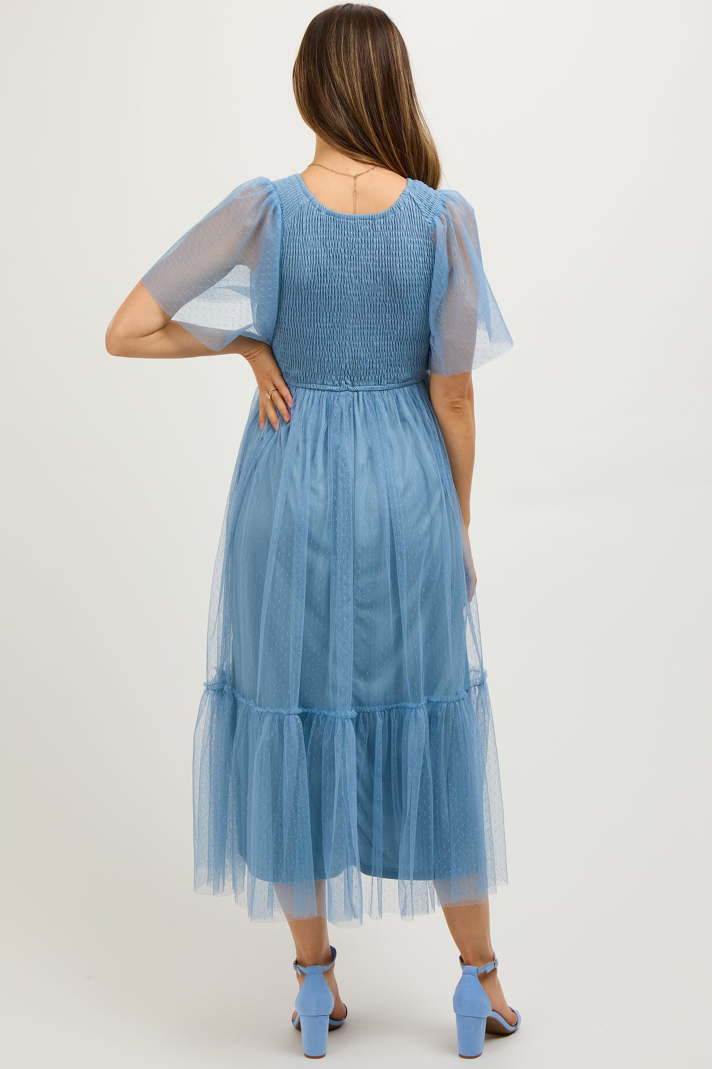 woman wearing a light blue maternity dress with puff sleeves and a tiered tulle skirt, showing a baby bump from behind