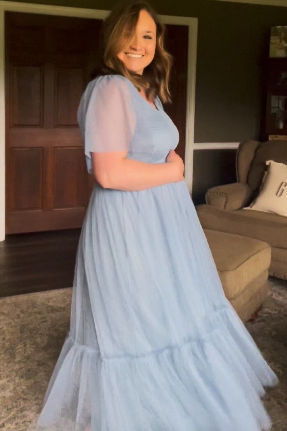 woman wearing a light blue maternity dress with sheer sleeves and a tiered skirt, holding her baby bump