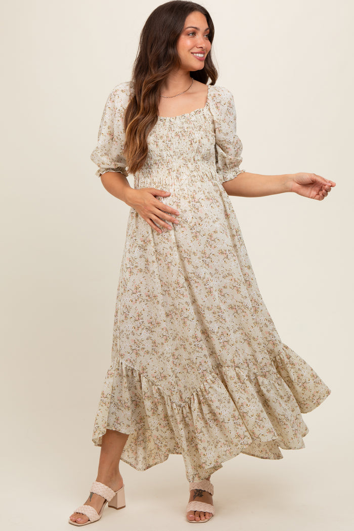 woman wearing a floral print maternity maxi dress with puff sleeves and a tiered hem, gently holding her baby bump