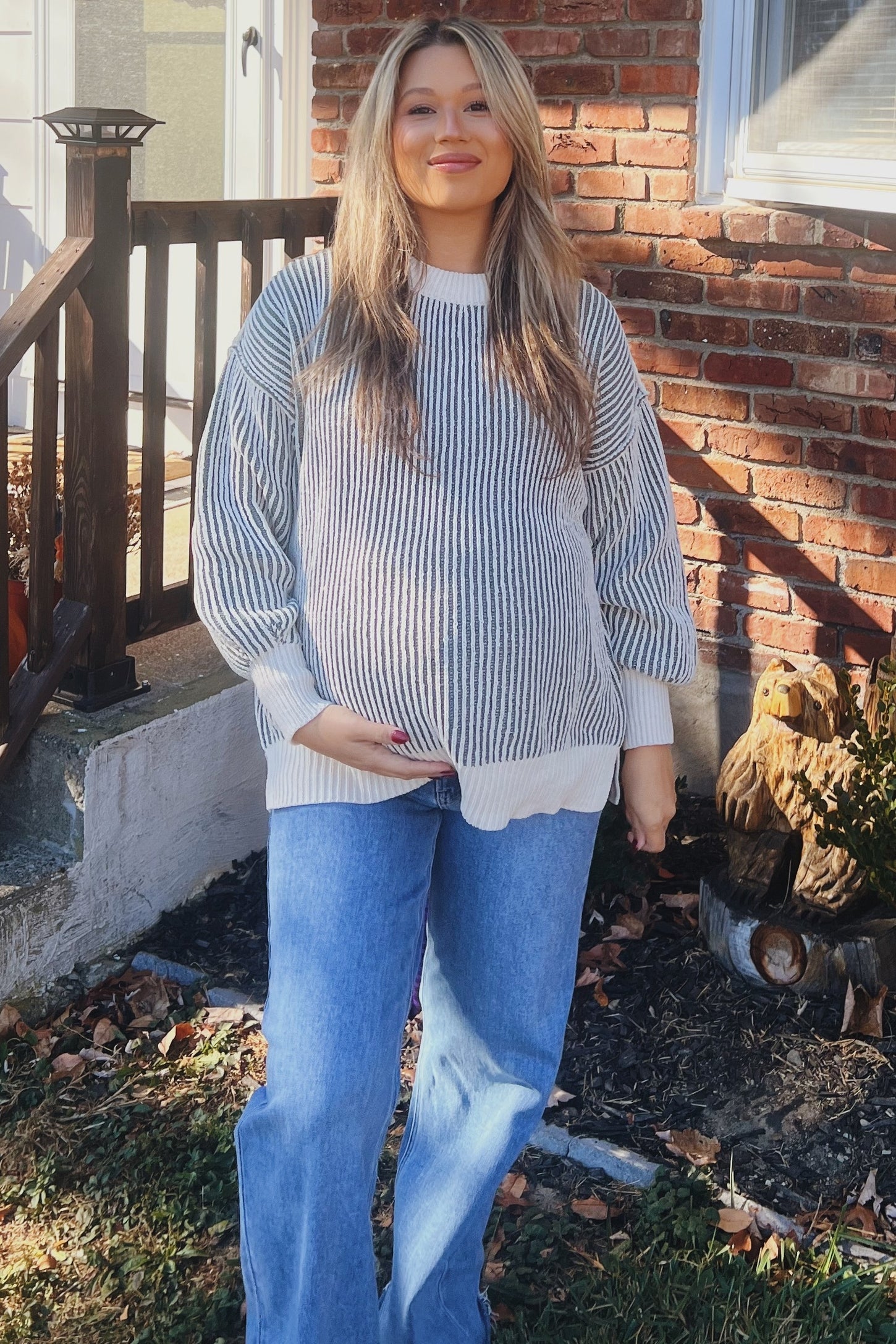 woman wearing a cream and grey striped maternity sweater and blue flared jeans, showing her baby bump