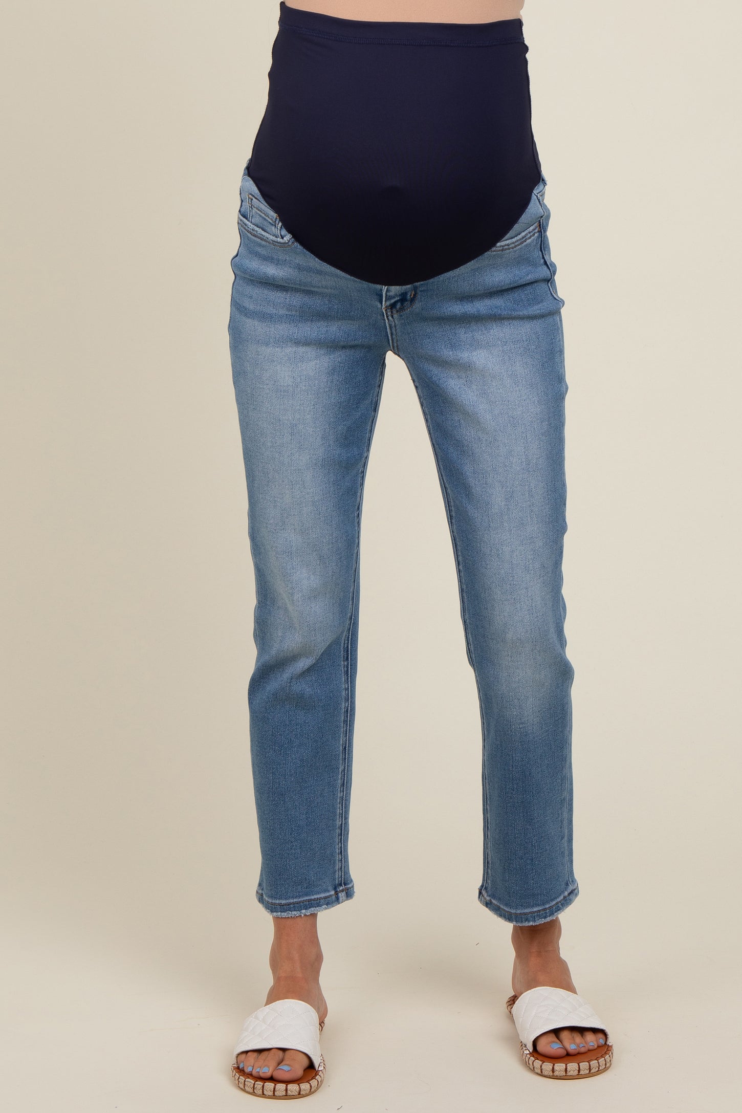 woman wearing light blue maternity jeans with a high navy belly panel and white slide sandals