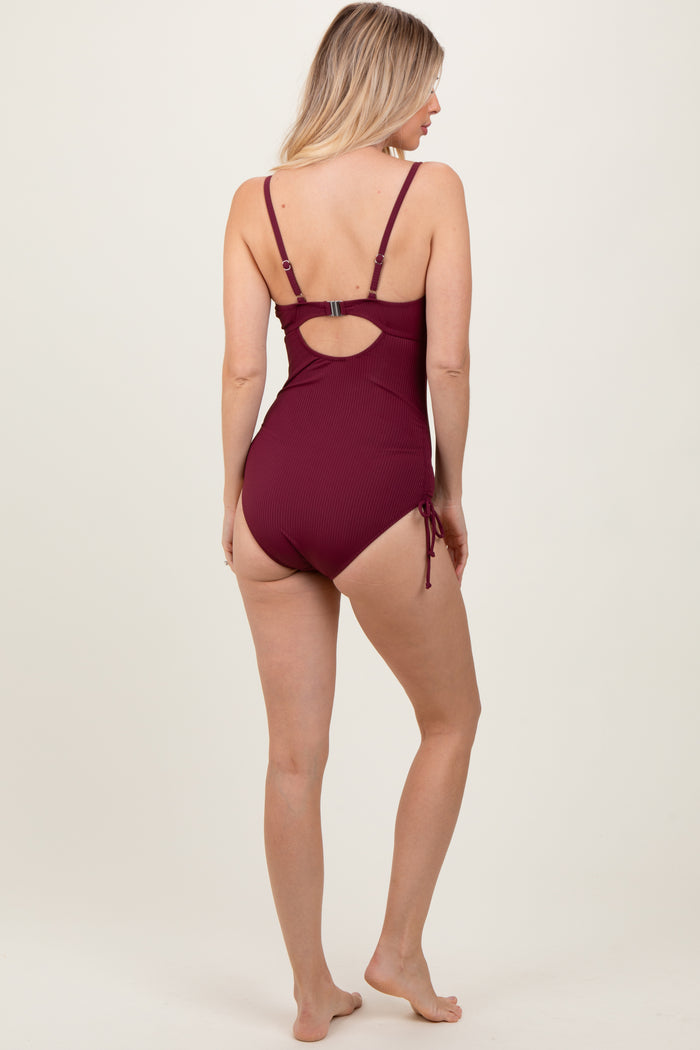 woman wearing a burgundy ribbed one-piece swimsuit with adjustable straps and side ties, viewed from the back