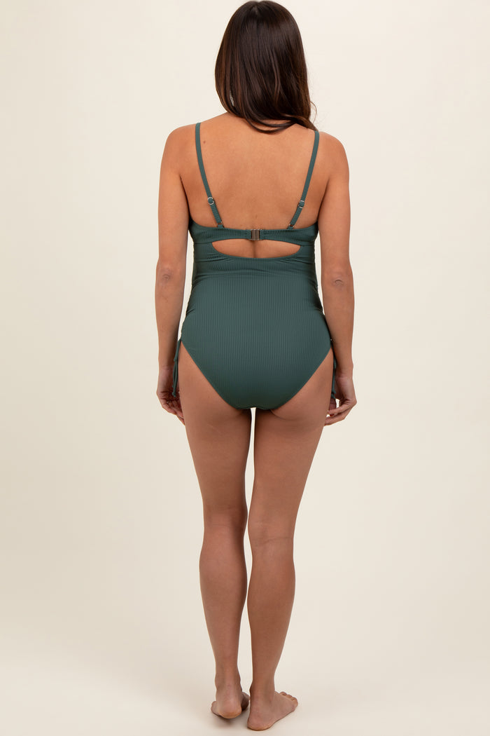 woman wearing a dark green ribbed maternity swimsuit with adjustable straps and a cutout back, showing her baby bump