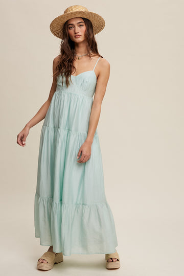 woman wearing a light green maxi dress with tiered ruffles and thin straps, styled with a straw hat and platform sandals