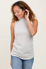 woman wearing a light gray ribbed sleeveless top and blue jeans, smiling and touching her hair