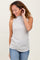 woman wearing a light gray ribbed sleeveless top and blue jeans, smiling and touching her hair