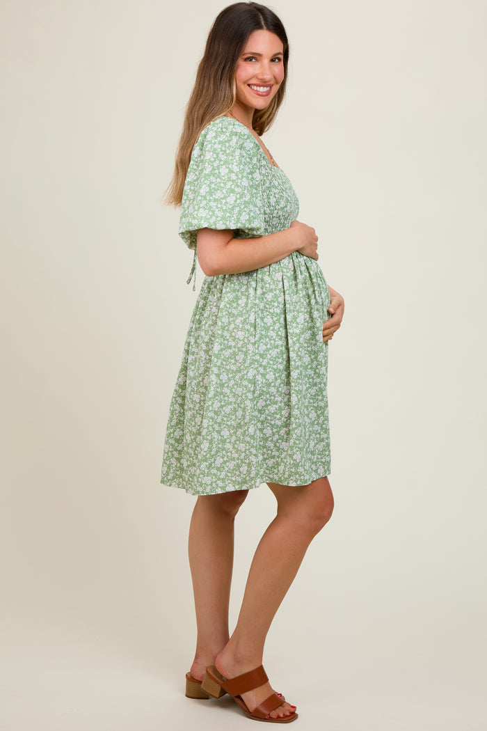 woman wearing a green floral maternity dress and holding her baby bump