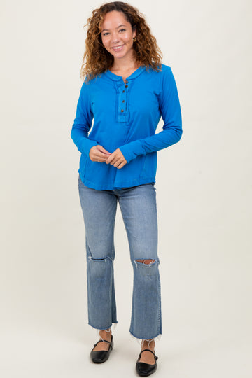 woman wearing a bright blue long sleeve henley top with buttons paired with light blue ripped jeans and black flats