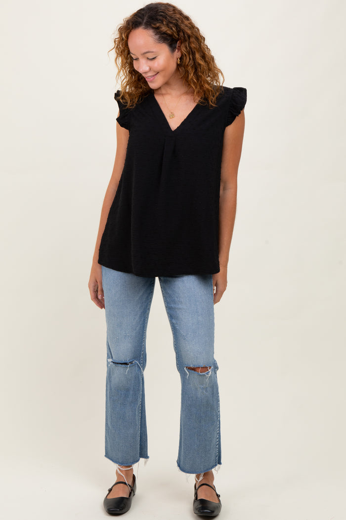 woman wearing a black ruffled sleeve top and distressed light blue flared jeans, standing and smiling