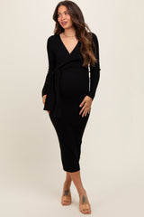 woman wearing a black ribbed maternity wrap dress with long sleeves and a tie at the waist, showcasing her baby bump