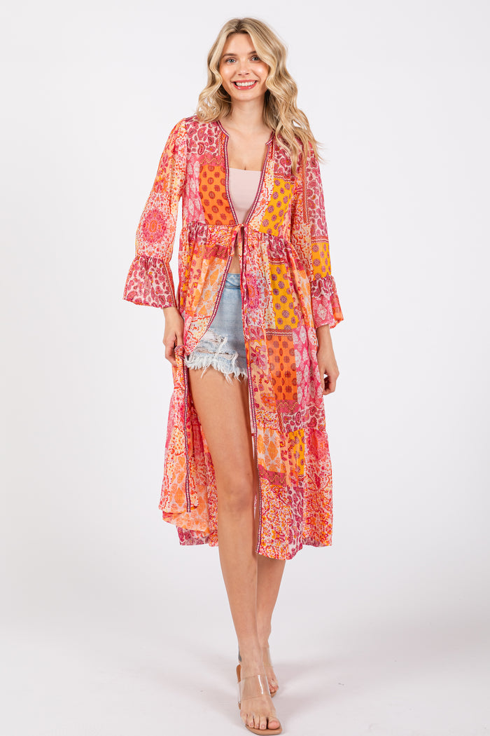 woman wearing a colorful patterned long kimono with bell sleeves over a pink tank top and denim shorts