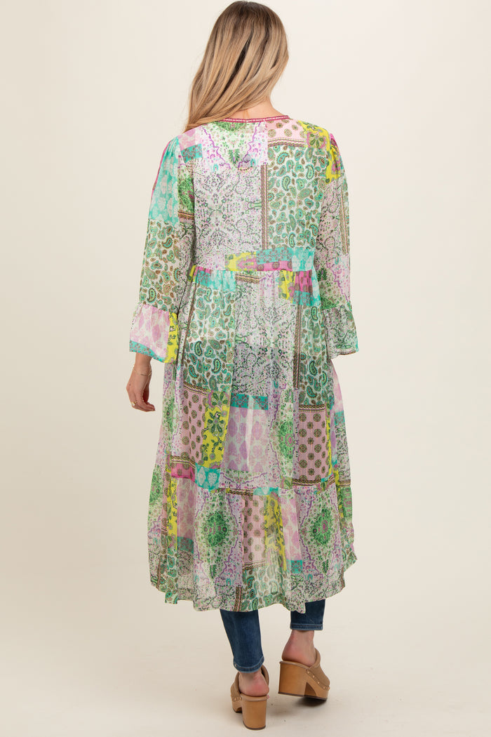 woman wearing a colorful patchwork long maternity dress with long sleeves and a tiered hem, seen from the back