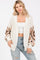 woman wearing a cream oversized crochet cardigan with colorful patterned sleeves and distressed light blue jeans