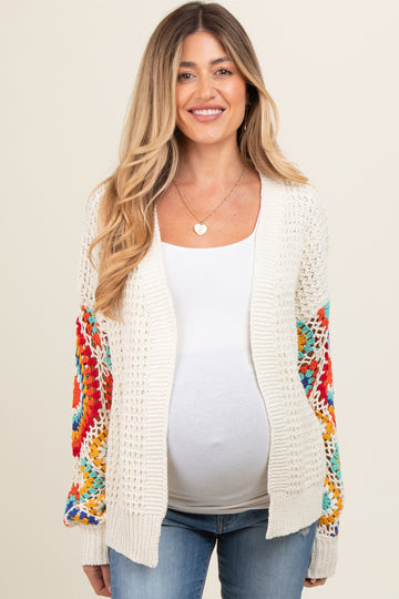 woman wearing a cream crochet maternity cardigan with colorful patterned sleeves and a visible baby bump