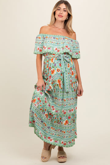 woman wearing a green off-the-shoulder floral maternity dress with a tie waist and a flowing maxi length