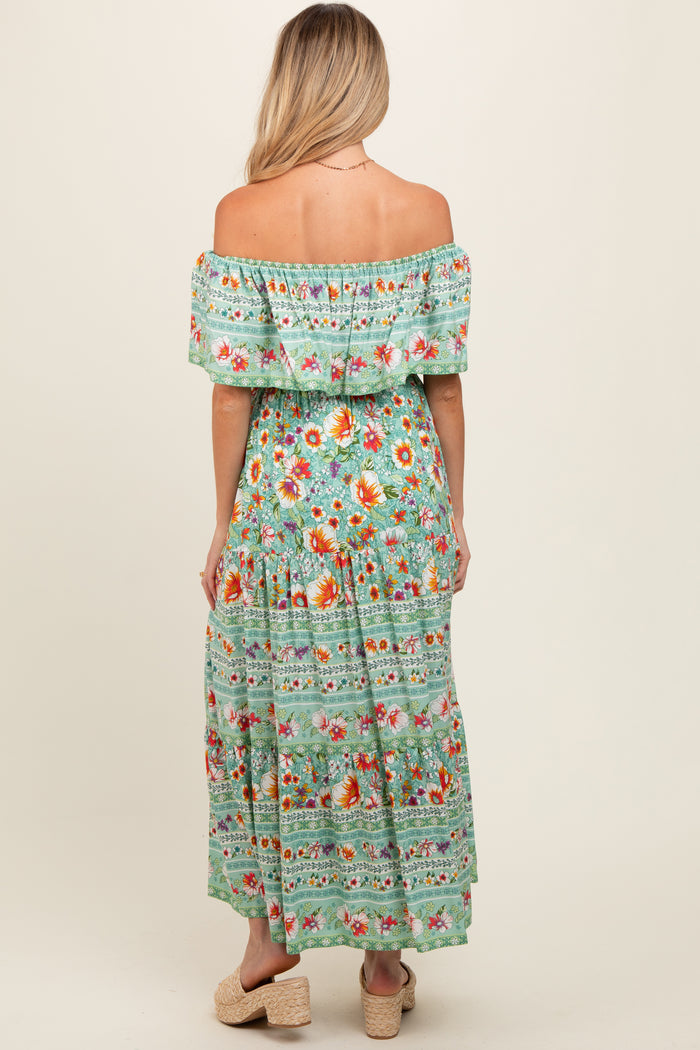 woman wearing a floral green off-the-shoulder maternity dress with a flowing skirt, showing her back