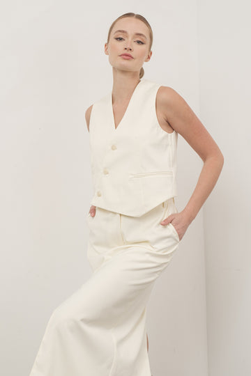 woman wearing an off-white sleeveless double-breasted vest with side pockets and matching high-waisted pants