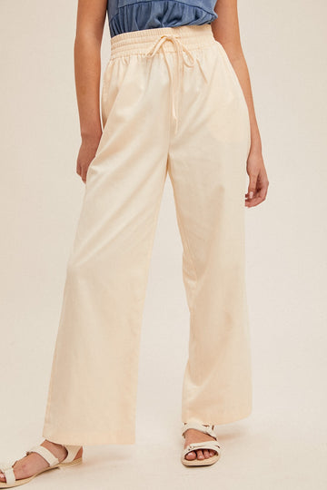 woman wearing cream wide-leg pants with an elastic waistband and drawstring, styled with a blue top